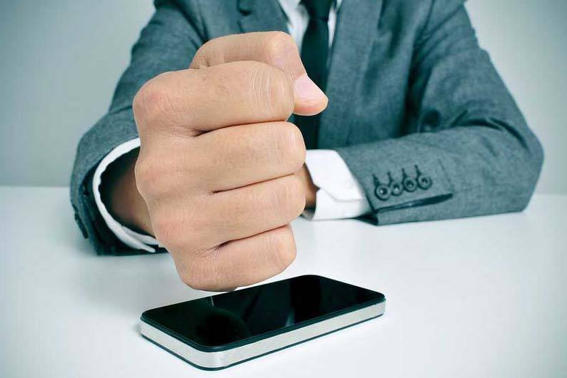 businessman hitting a cell phone with his fist